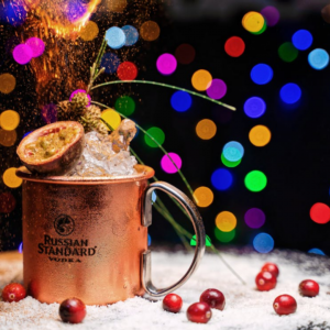 Festive holiday cocktail in a copper mug at a Christmas pop-up bar near the NJ Shore, surrounded by colorful lights and cranberries.